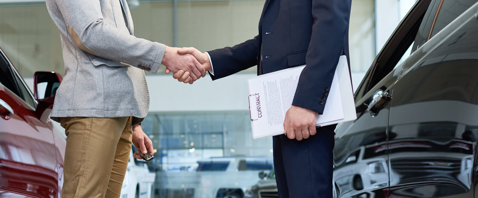 Two people shaking hands between showroom cars at a dealership