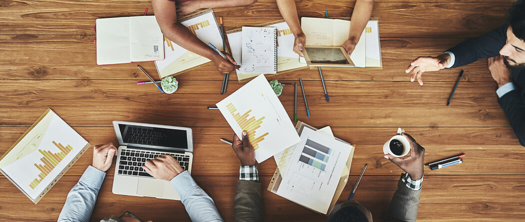 Top-down view of a meeting desk with various papers and technology on top