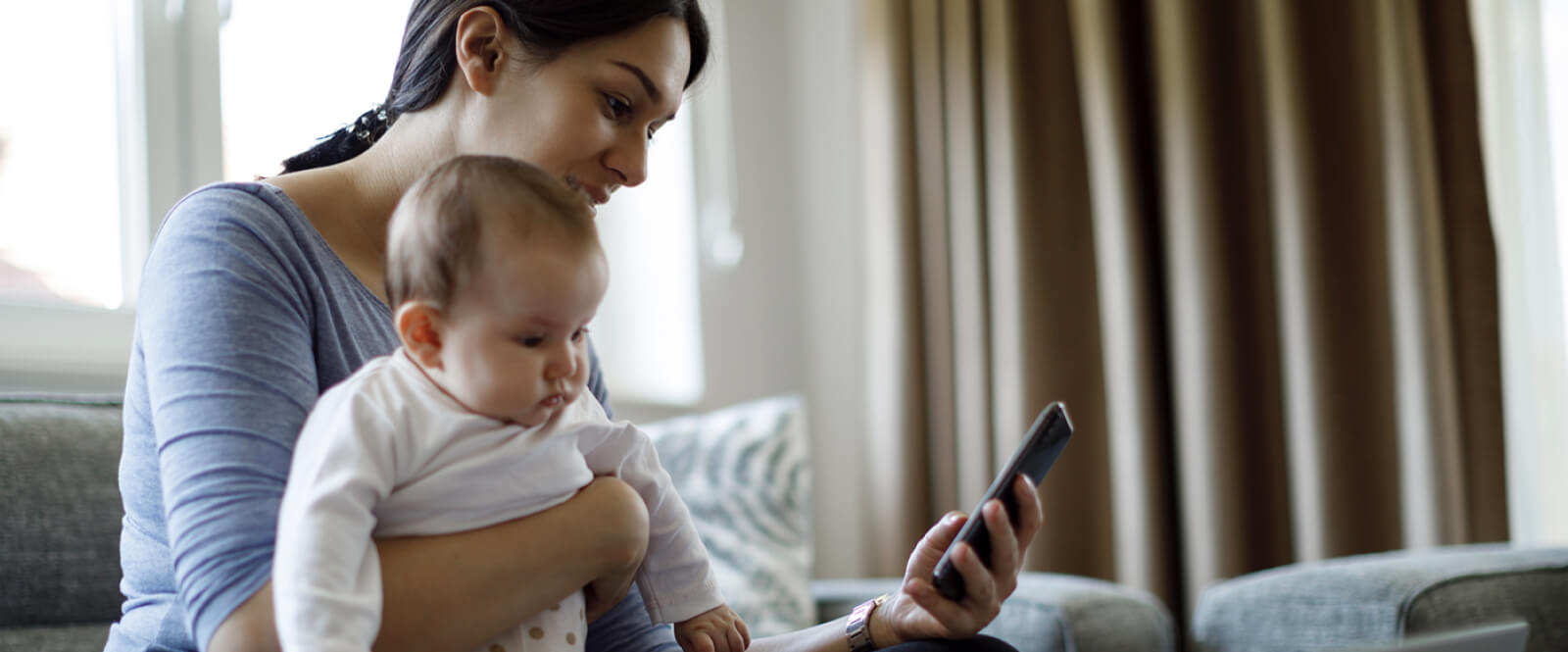 Young woman holding an infant and looking at a smartphone