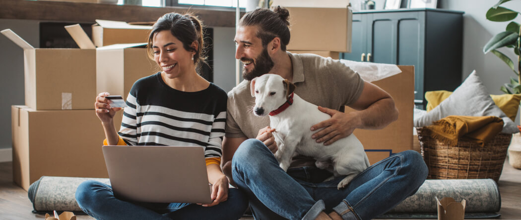 Young couple surrounded by moving boxes looking at a laptop and credit card